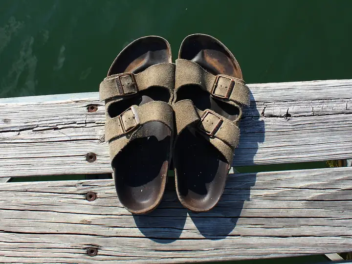 A pair of cork-footbed sandals with two buckled straps on a weathered wooden dock