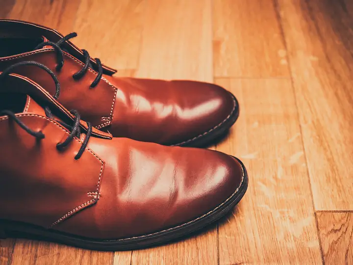 A pair of polished brown leather lace-up shoes on a wooden floor