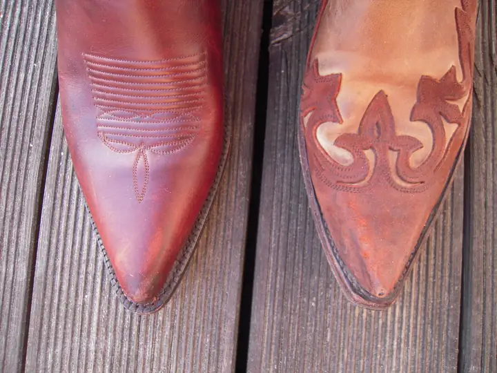 The pointed toes of two worn cowboy boots with decorative stitching