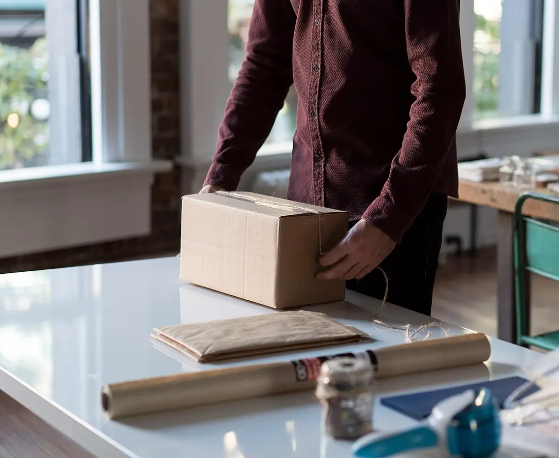 A person taping up a cardboard box on a white table
