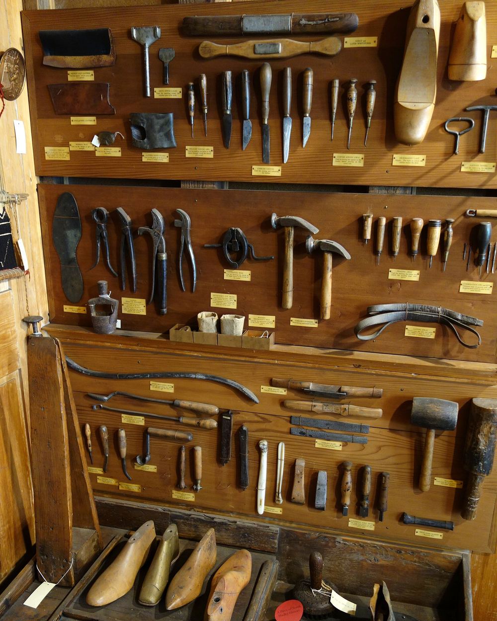 Rows of old shoemaker’s tools mounted on dark wooden boards: knives, awls, pincers, hammers and wooden lasts