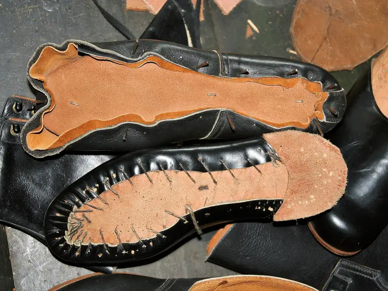 Black leather uppers nailed and stitched to tan insoles, seen from the sole side